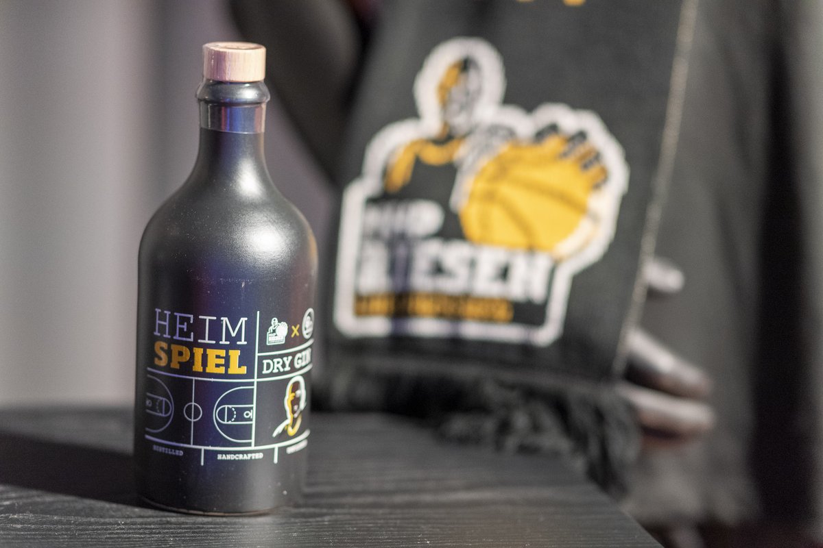Flasche „Heimspiel Dry Gin“ vor dem Logo der MHP RIESEN