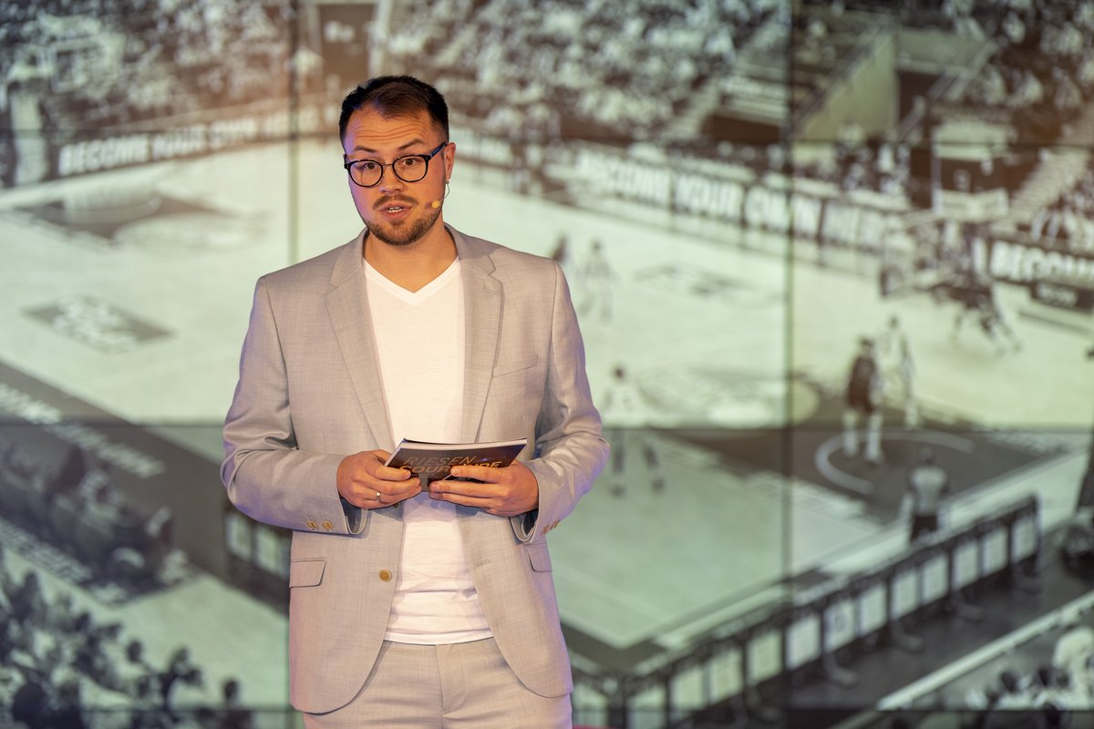 Moderator Florian von Stackelberg auf der Bühne vor einer Basketball-Projektion