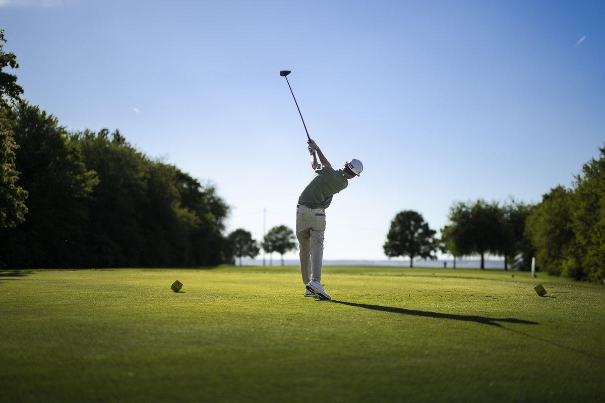 Spieler beim Abschlag im Gegenlicht, langer Schatten auf dem Fairway