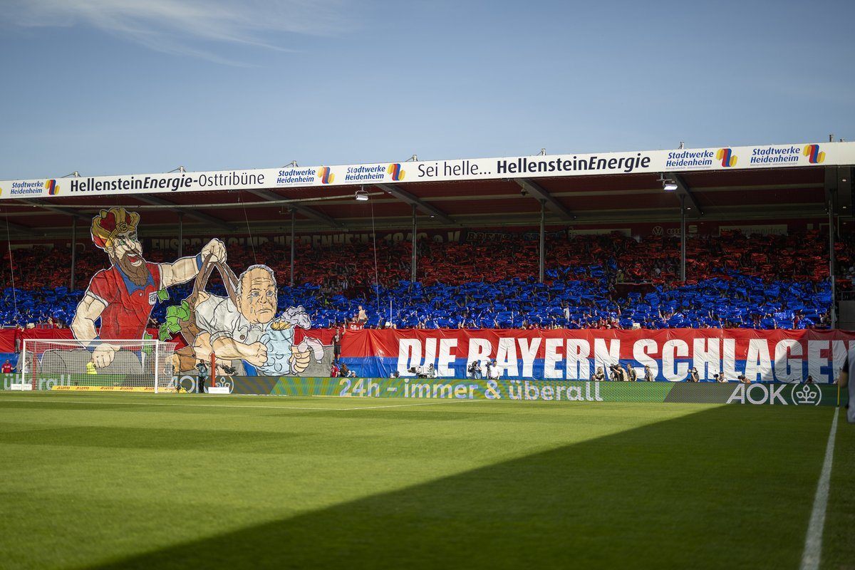 Choreografie der Heidenheimer Fans über die ganze Tribüne mit dem Banner „Die Bayern schlagen“
