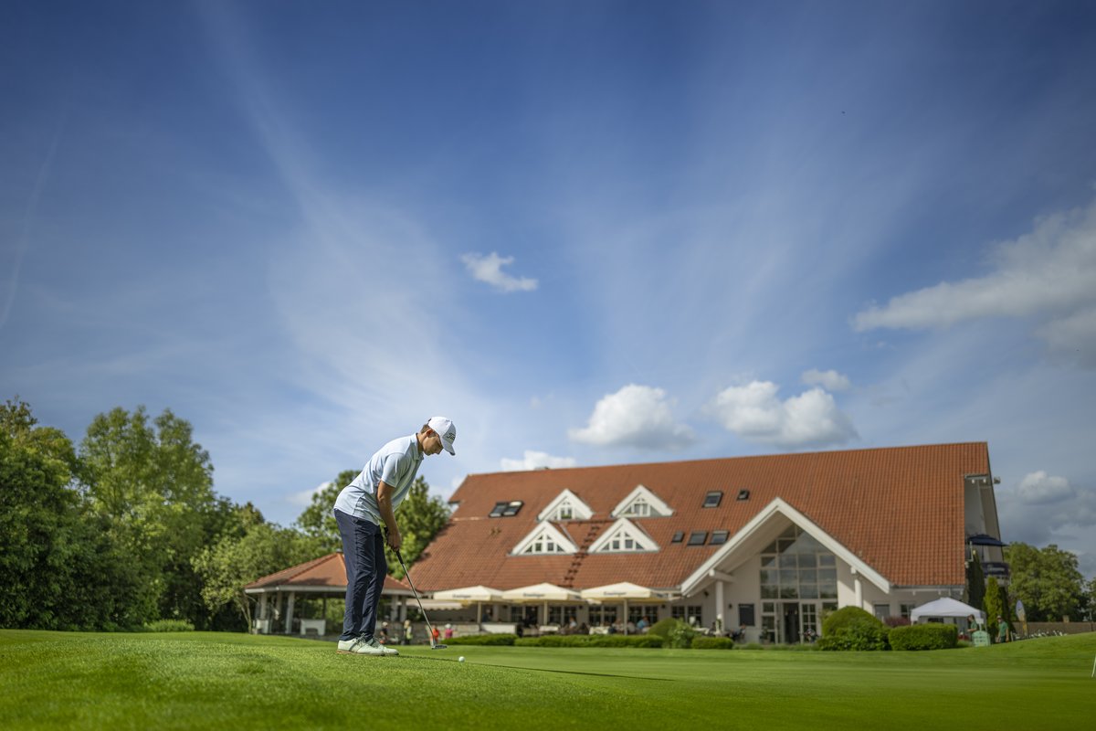 Golfer beim Abschlag vor dem Clubhaus unter weitem Himmel