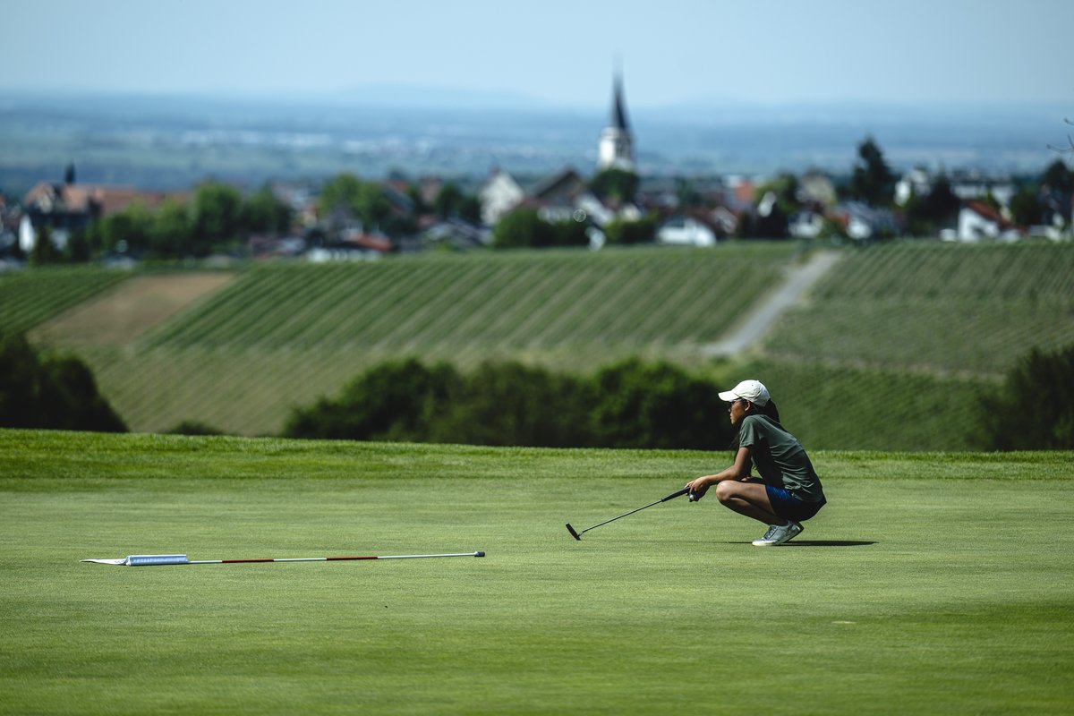 Spielerin liest das Grün, dahinter Weinberge und Ort