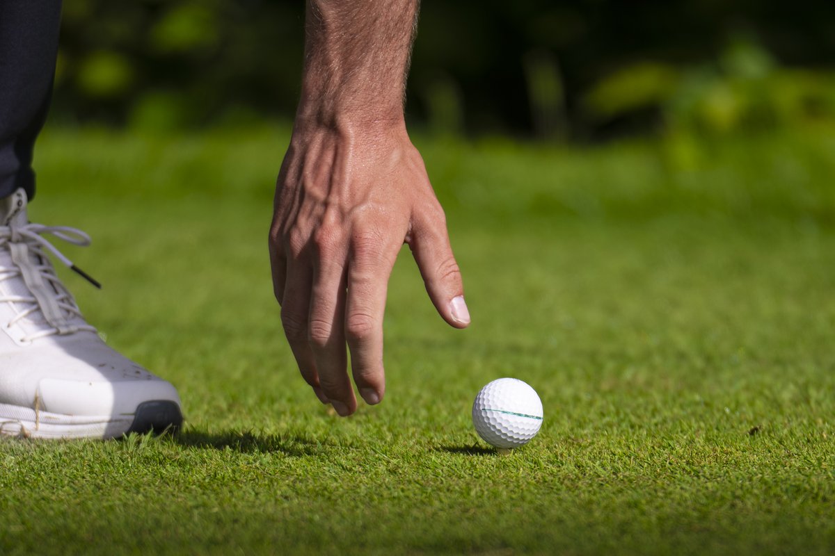 Hand legt einen Golfball auf das Grün