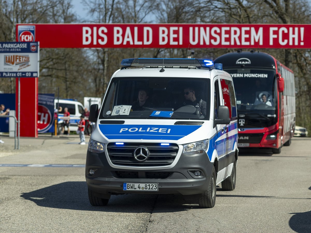 Polizeifahrzeug und Mannschaftsbus des FC Bayern München fahren unter dem Banner „Bis bald bei unserem FCH!“ vor